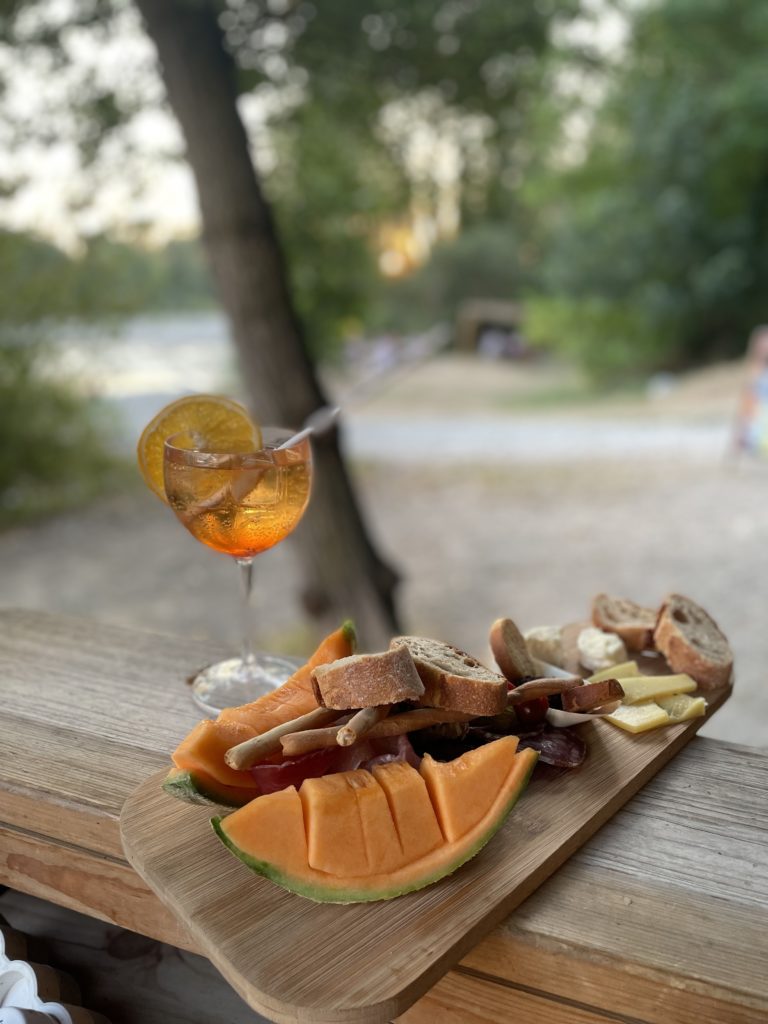 Planche apéritif avec du melon, du fromage, de la charcuterie, du pain et un cocktail.