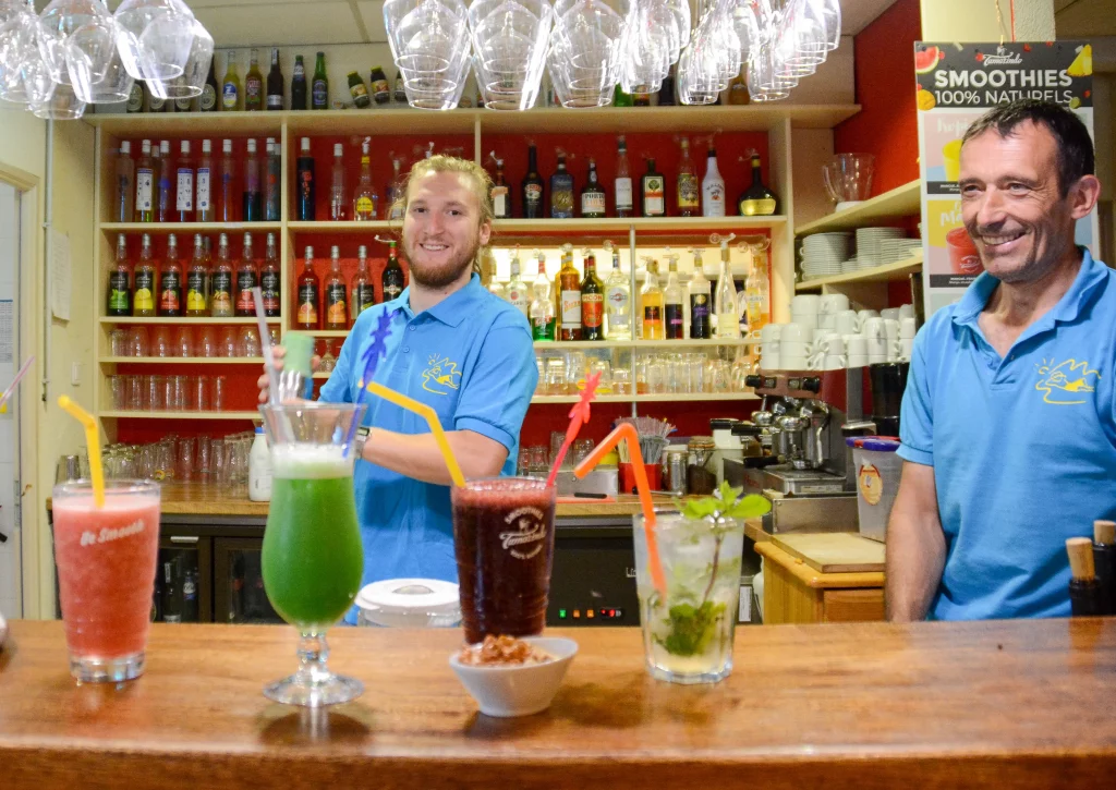 Comptoir du bar, avec 4 cocktails et deux barmans en second plan